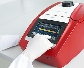 a gloved hand operating the touchscreen on a Biometra TAdvanced thermal cycler